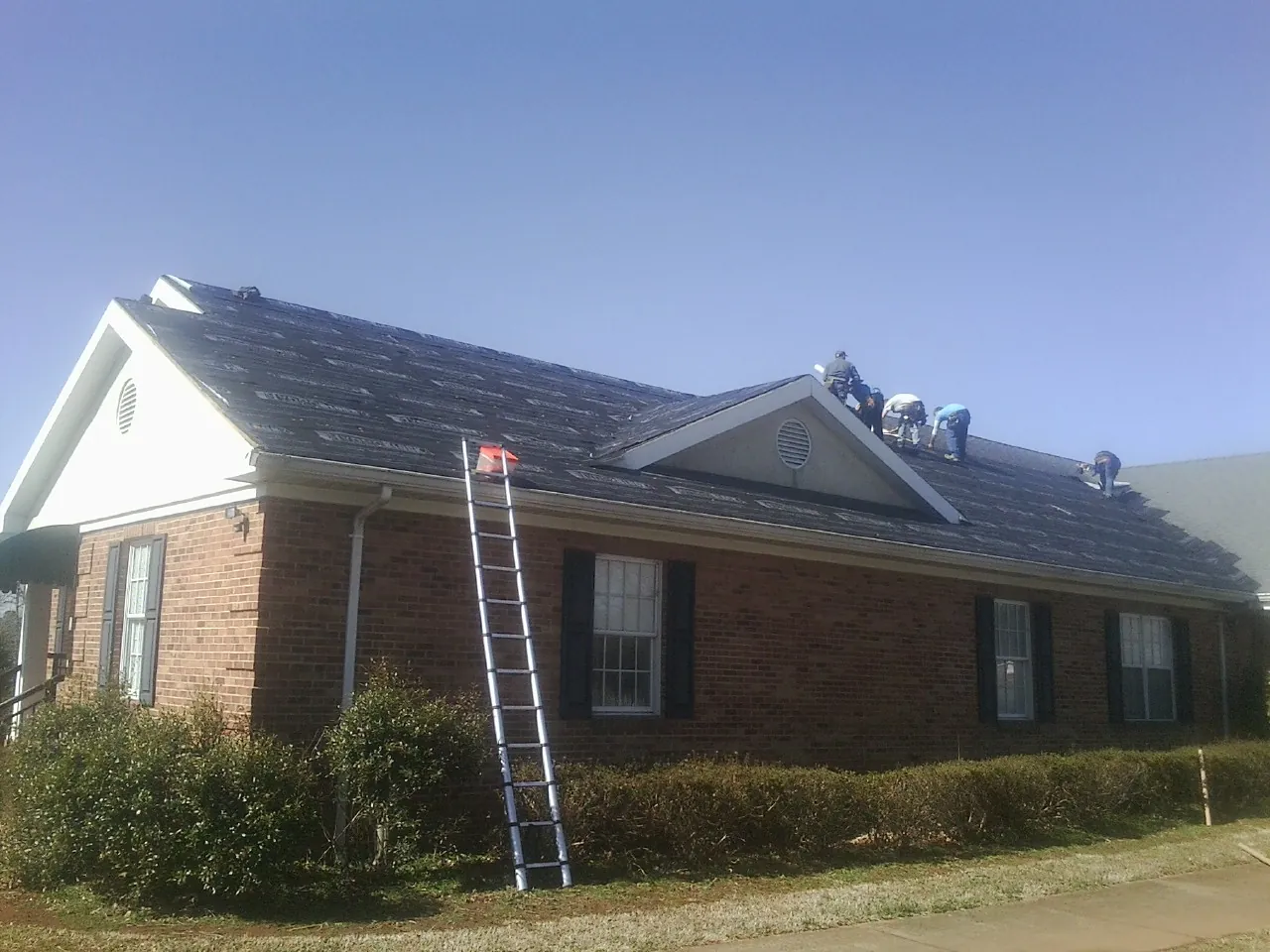 Crew tearing shingles off a brick ranch roof with a ladder set — Metal Roof Repair work by our crew in Whittier