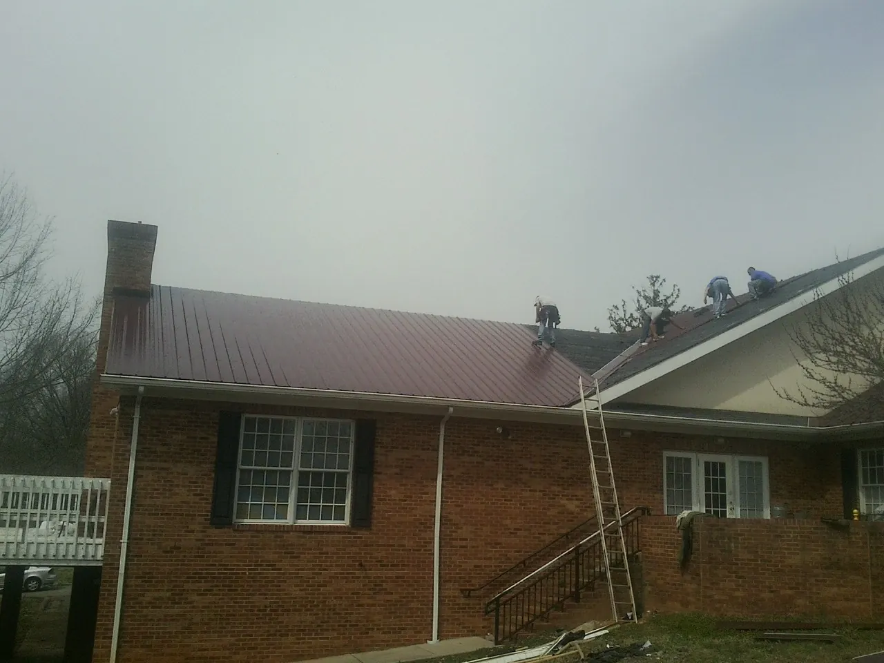 Crew setting red metal roofing panels on a brick home in Whittier