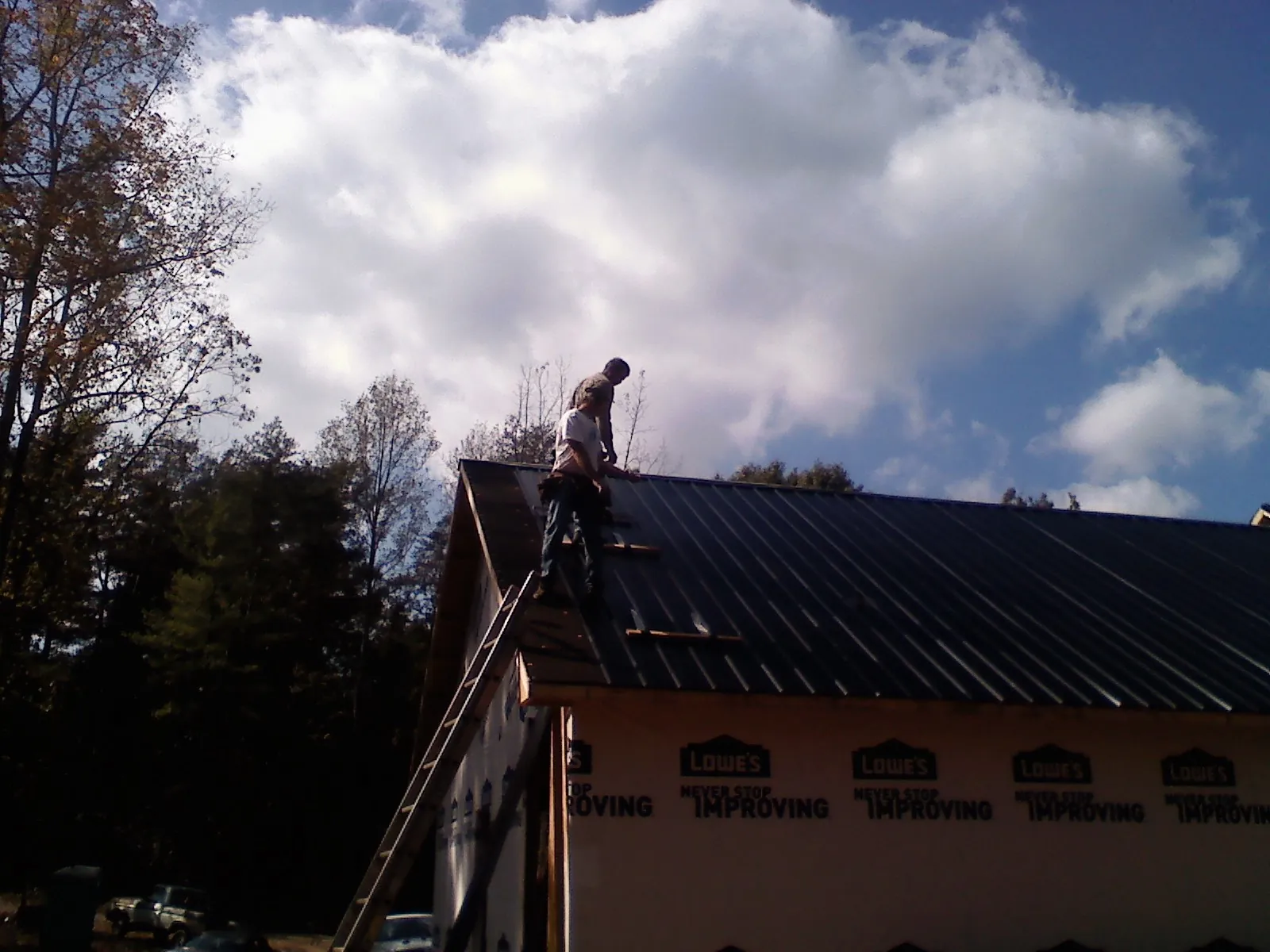 Roofer fastening dark metal panels high against a cloudy sky, from a Roof Inspection job in Whittier